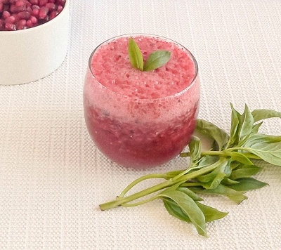 A glass filled with plum pomegranate smoothie and fresh basil as the prop