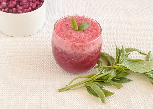 A glass filled with plum pomegranate smoothie and fresh basil as the prop