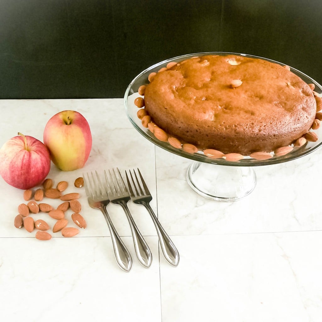 A full view of Apple cake with apples and raw almonds as the props