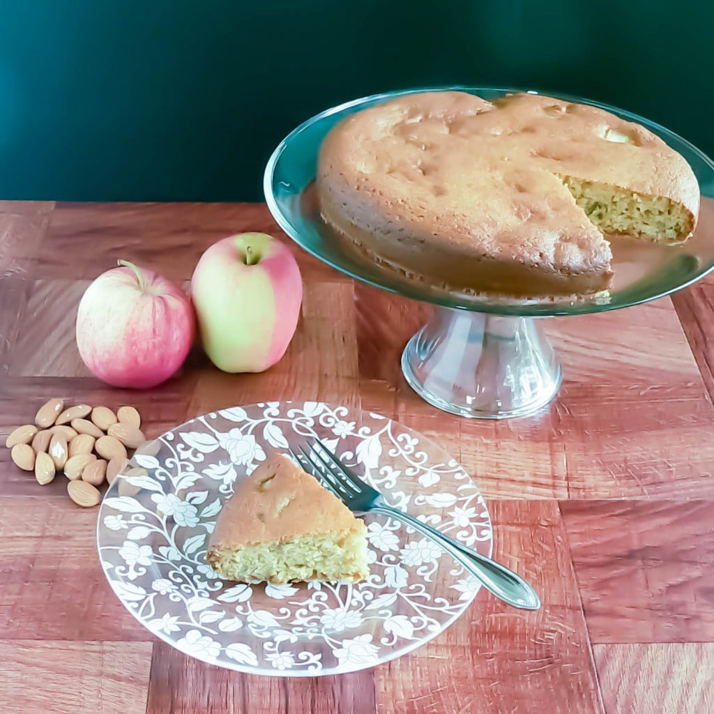 A slice of apple cake on a plate with the left over cake in the background
