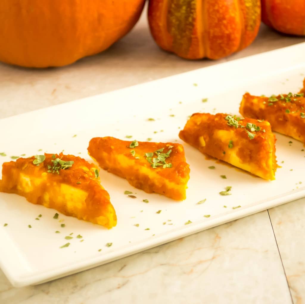 baked paneer in pumpkin sauce served in a long serving plate with pumpkins at the backdrop