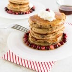 A stack of caramelized cranberries coconut pancakes topped with whipped cream