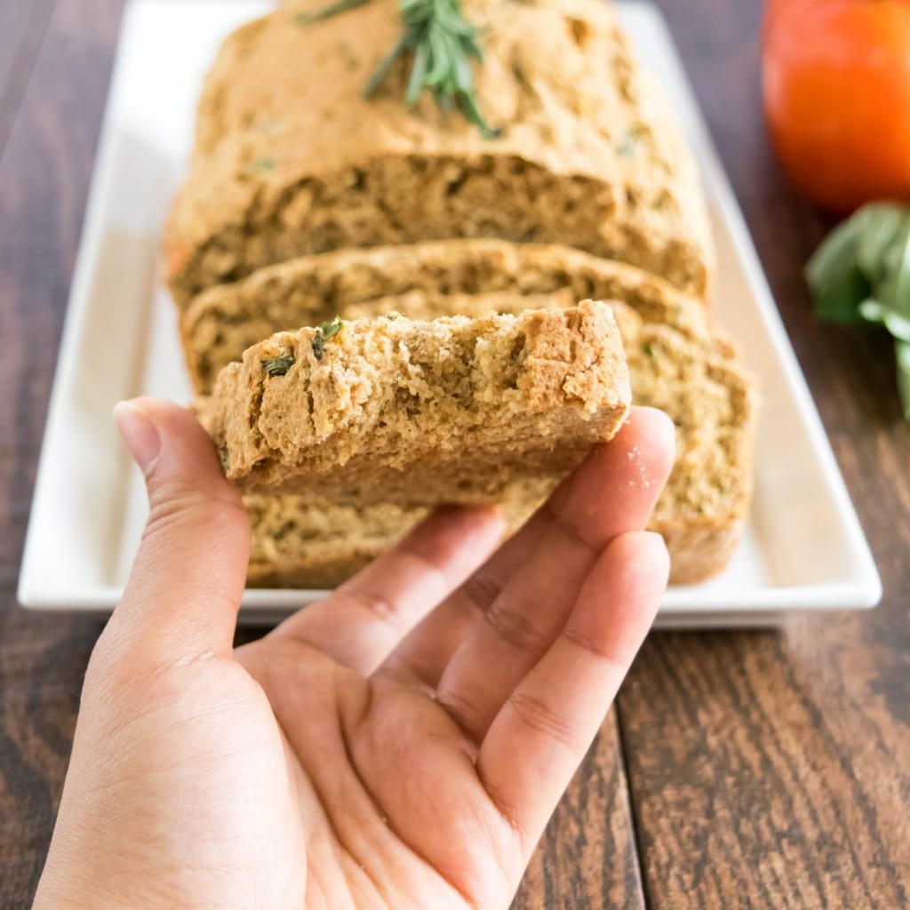 a hand holding sliced tomato herbed spelt bread