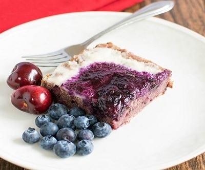 A 45 degree angle view of cherry oats squares with macadamia nut icing and blueberry sauce