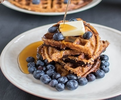 Syrup pouring over stacked peanut butter bulgur waffles