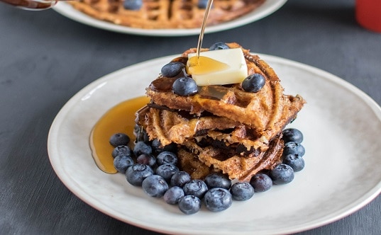 Syrup pouring over stacked peanut butter bulgur waffles