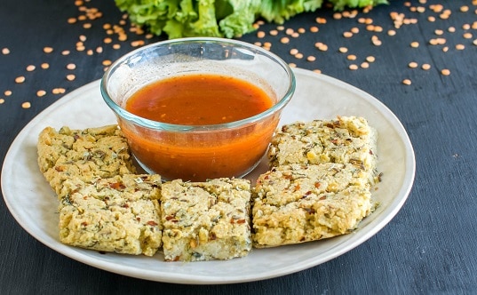 A plate full of lentil mustard green sticks along with tomato sauce