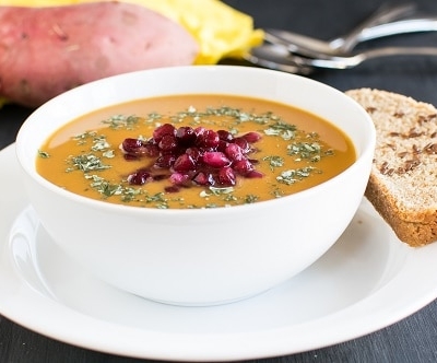 A front view of sweet potato pomegranate soup with a bread on the side