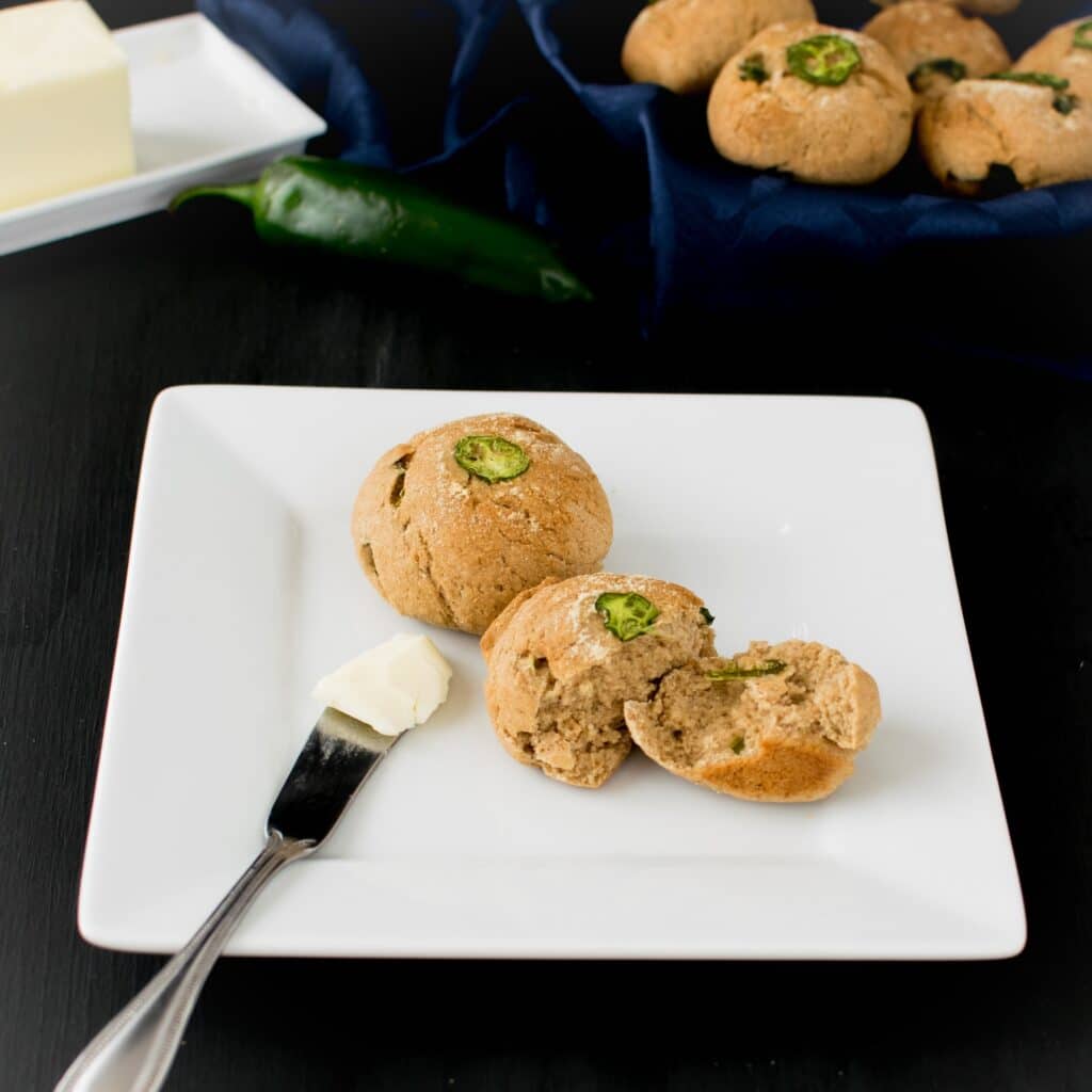 A 45 degree angle view of the broken dinner rolls on a plate with butter knife.