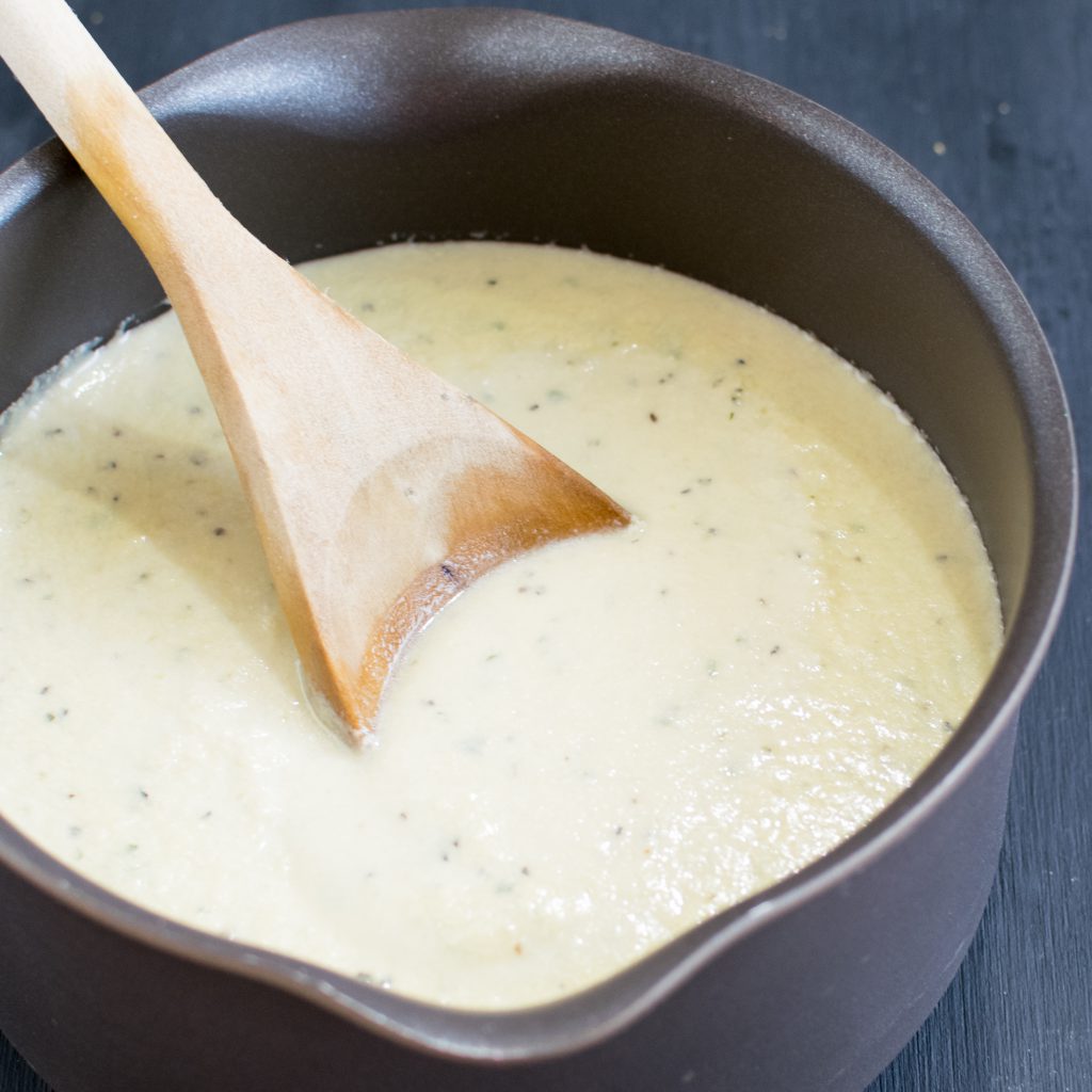 Vegan Cheese Sauce is shown in a pan with a wooden spatula