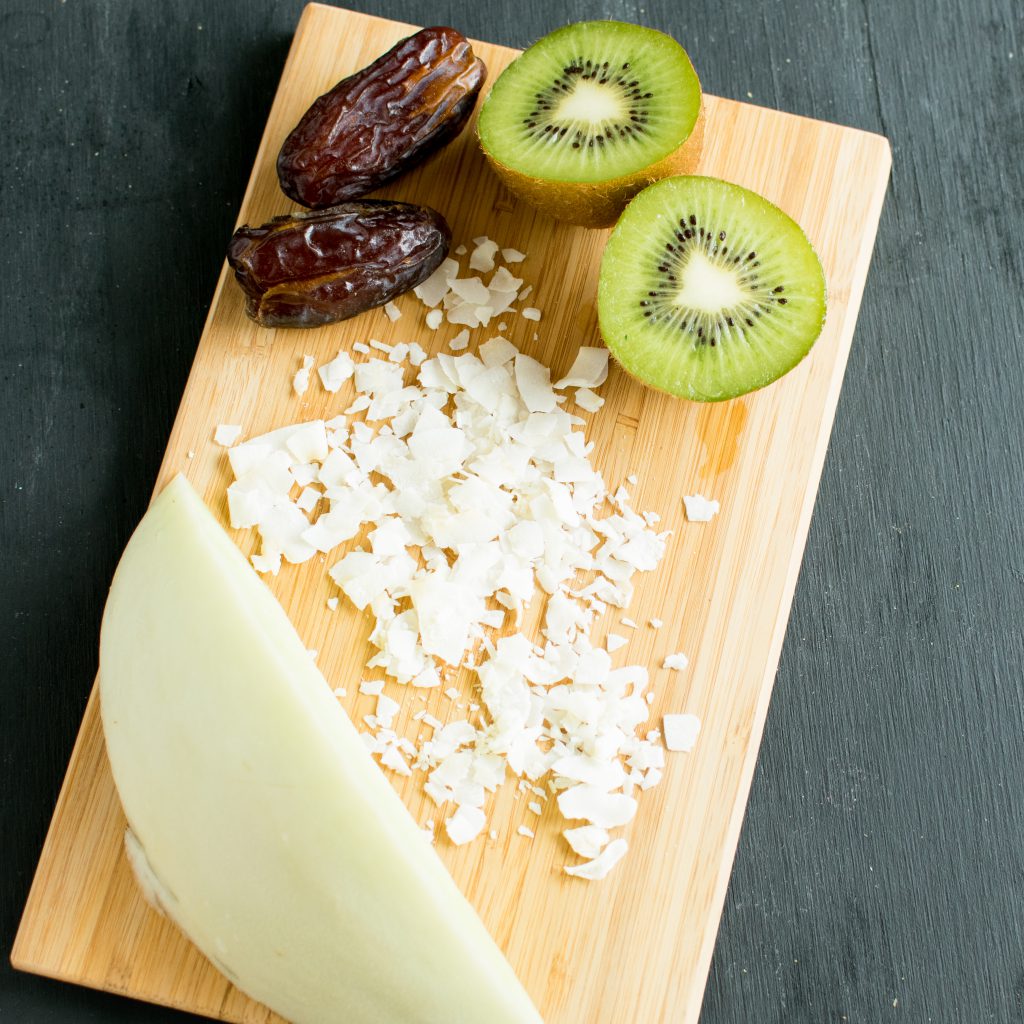 All the ingredients of Kiwi Honeydew Coconut Smoothie is shown on a wooden board.
