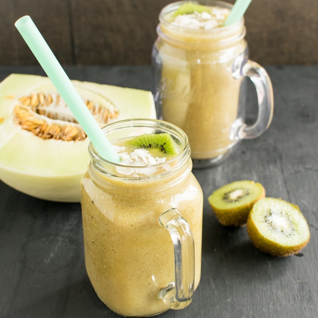Kiwi Honeydew Coconut Smoothies shown in the serving glasses with the ingredients as the prop.
