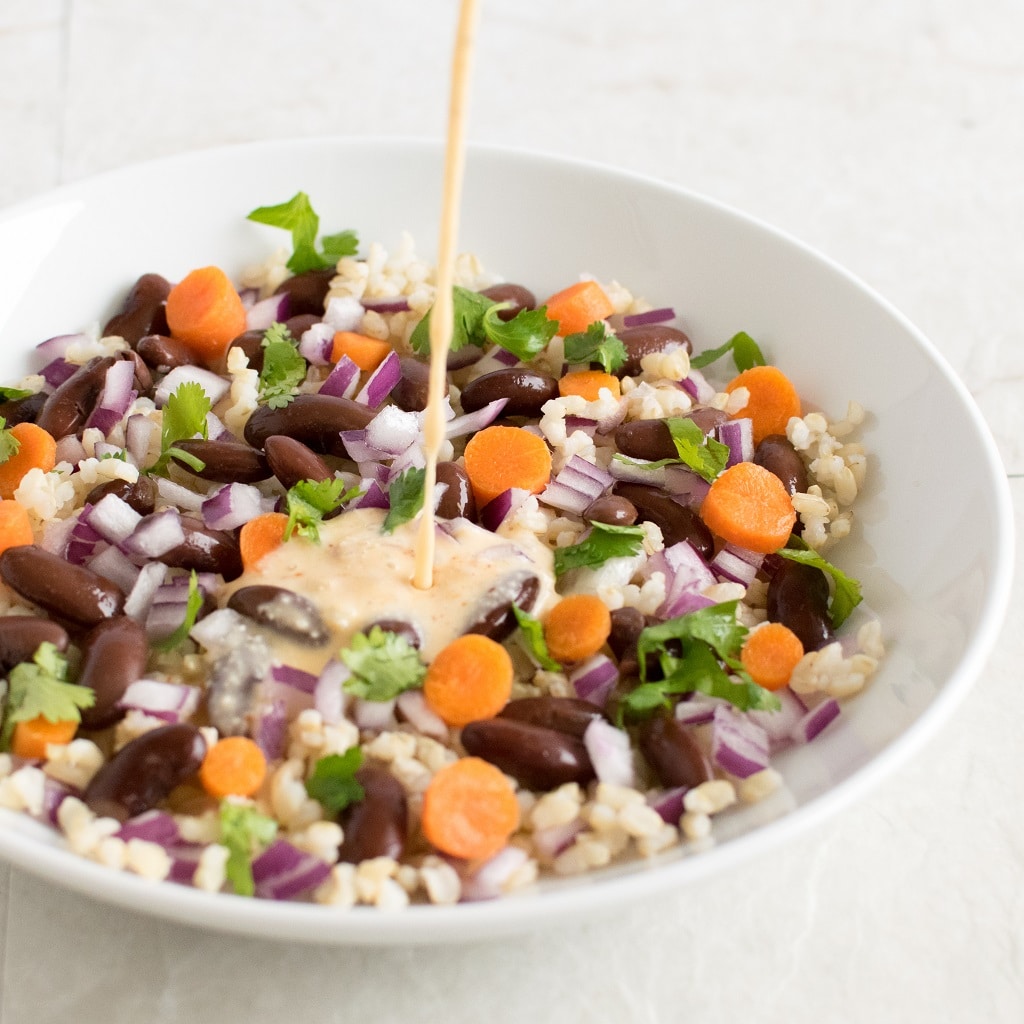 Brown Rice Kidney Bean Salad with Coconut Sriracha Dressing with the pouring dip