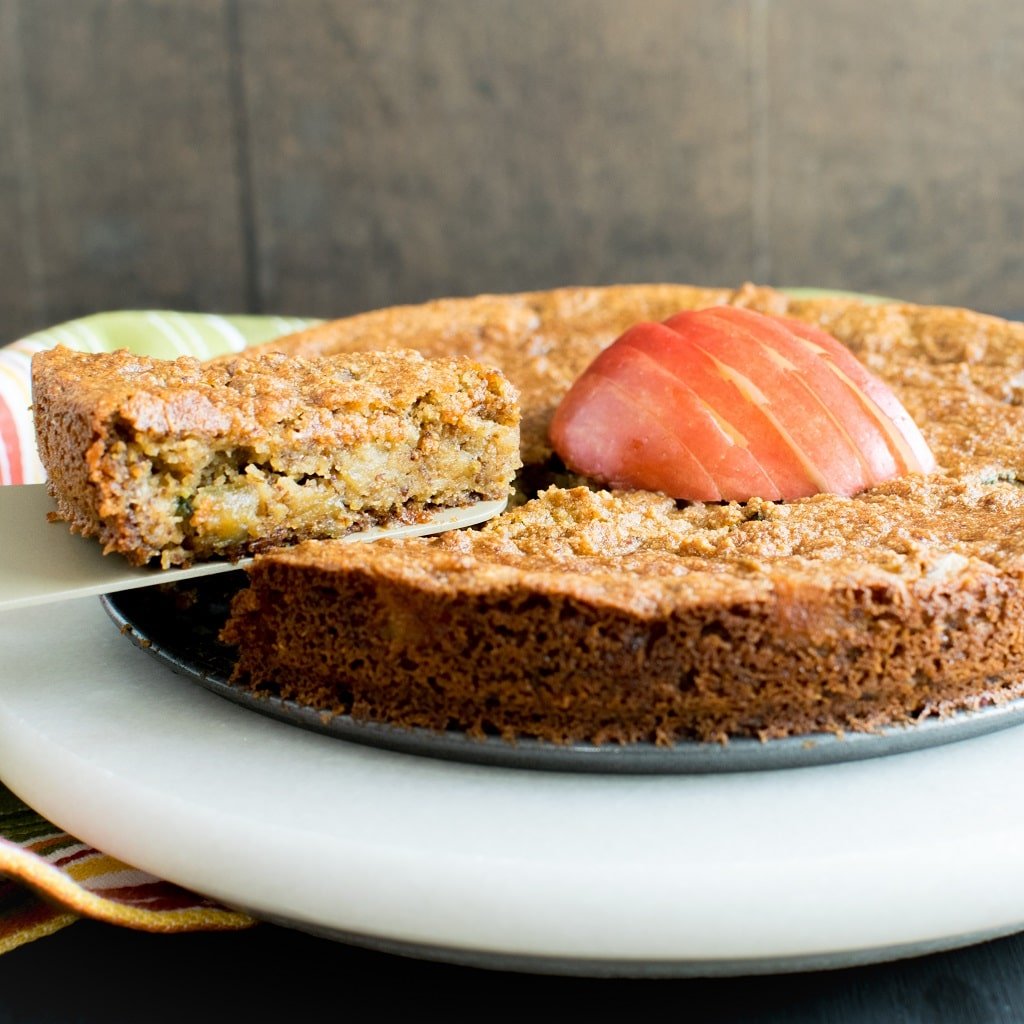 A slice of Pan Seared Vegan Apple Almond Cake is being lifted with a cake spatula