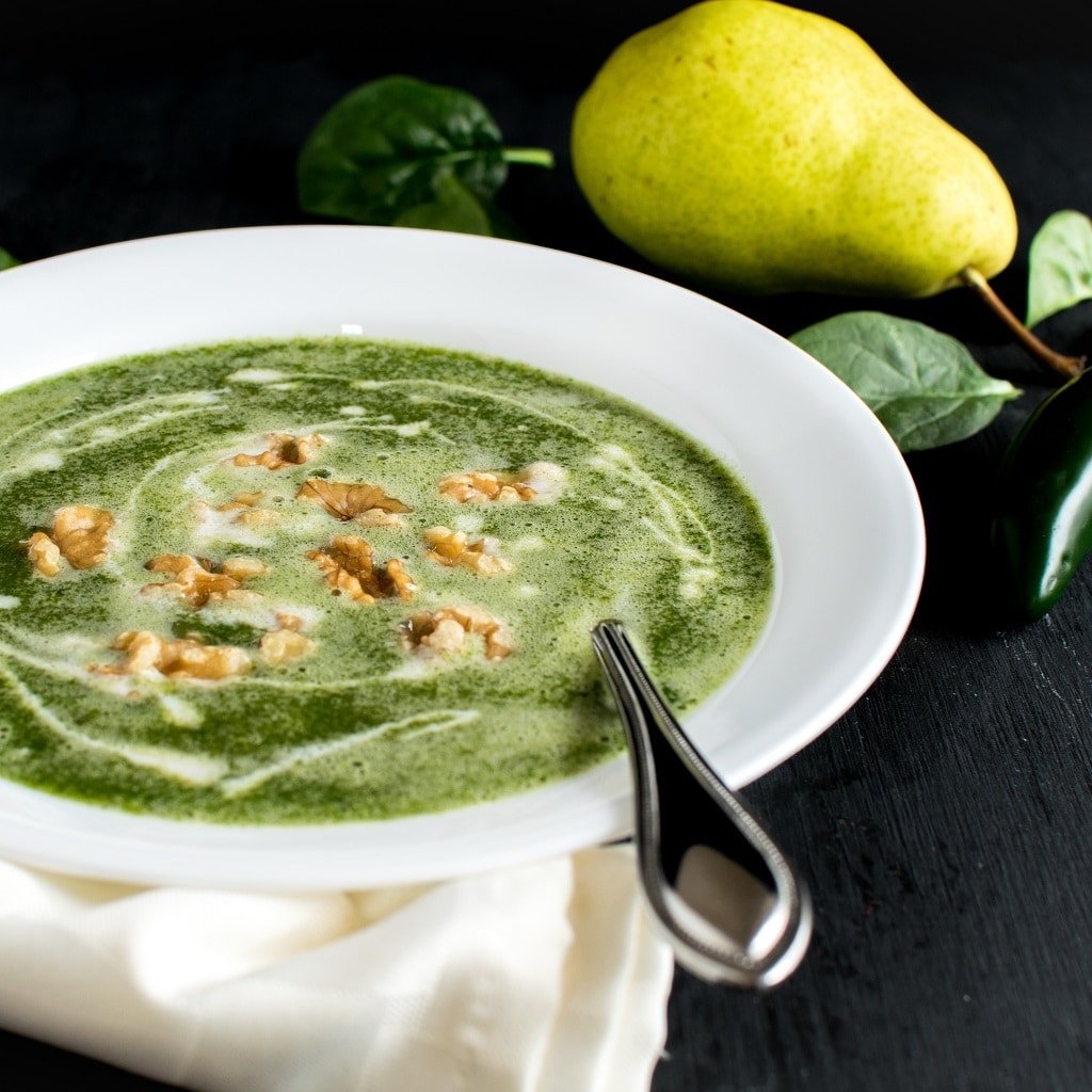 Fire Roasted Jalapeno Pear Spinach Soup is shown in a white soup bowl with the ingredients as the prop