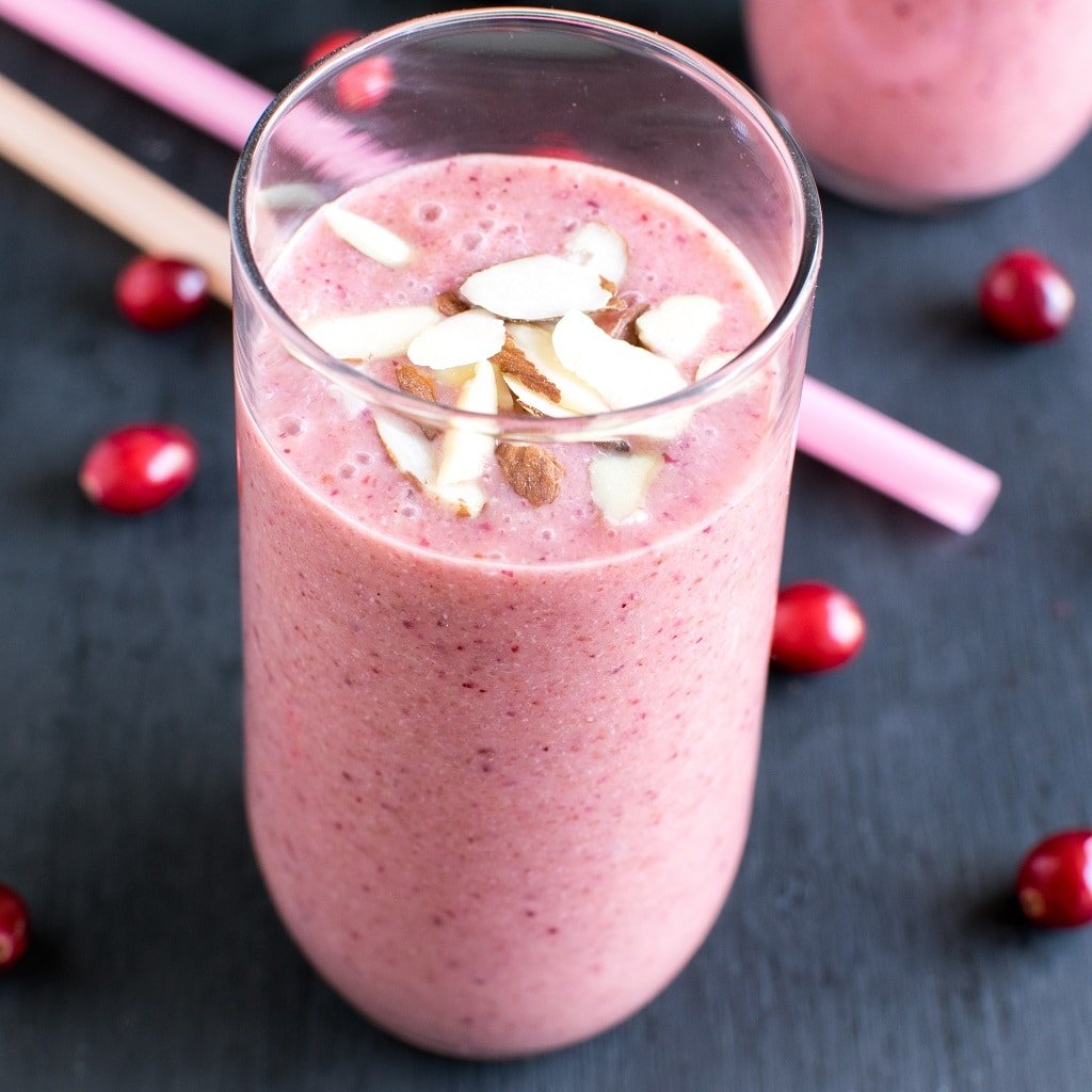 A glass filled with Cranberry Amaranth Smoothie with the straws and fresh cranberries as the prop.