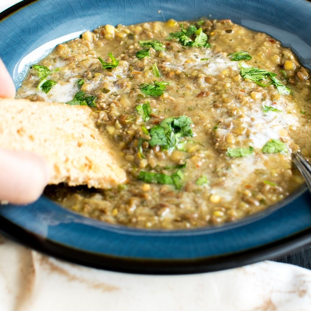 A hand holding the bread and dipping into Lentil Cilantro Soup is shown here [ vegan + gf ] kiipfit.com