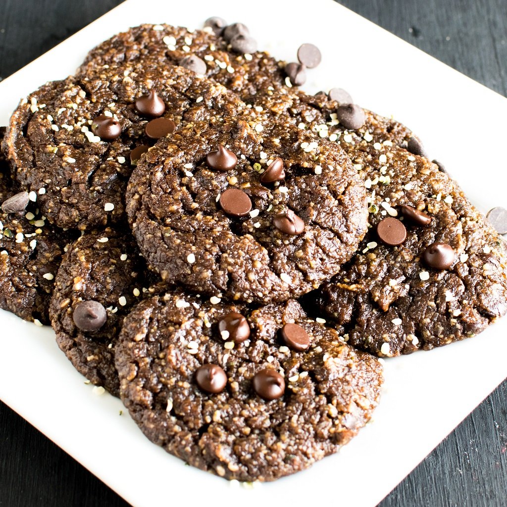 Lots of chocolate cauliflower protein cookies are shown on a white square plate with choclate chips on the top and hemp sees sprinkled all over the cookies | kiipfit.com