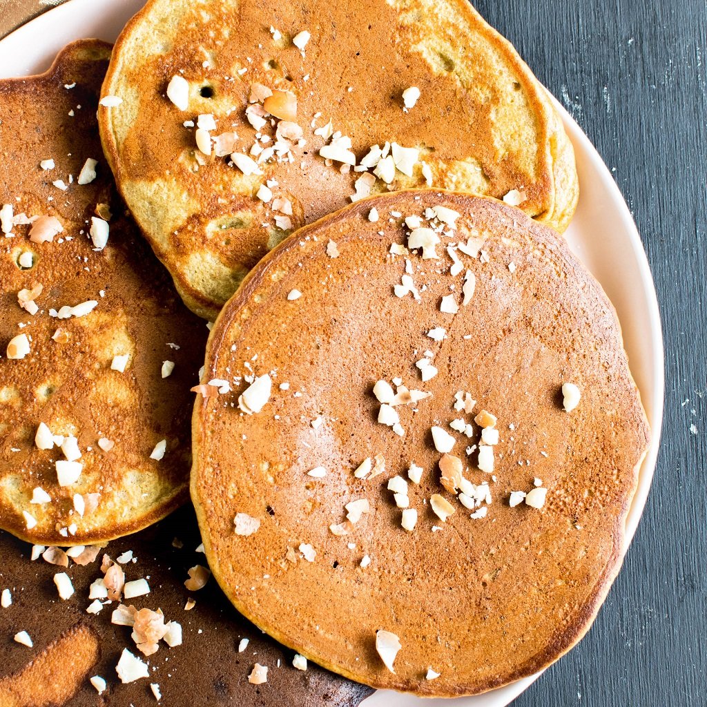 A plate full of the pancakes topped with peanuts in shown in this image