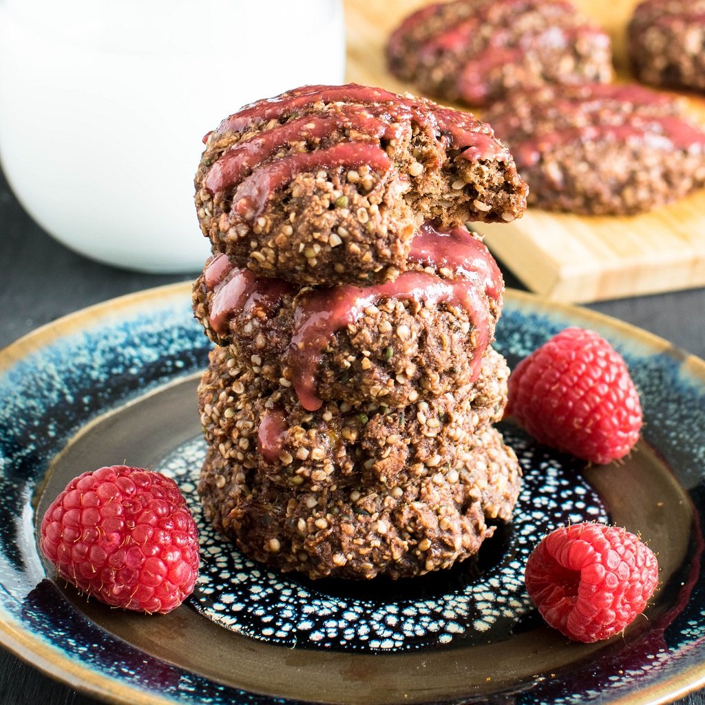 A tall stack stack of Raspberry Glazed Chocolate Oatmeal Cookies with half a cookie at the top of the stack and lots of cookies and a glass of milk as the prop is shown in this image | kiipfit.com 