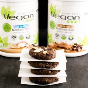 A stack of cookies with parchment paper between them and protein powder boxes at the background is shown in this image.