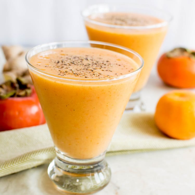 Immune Boosting Persimmon Ginger Smoothie is shown in the serving glasses with all its ingredients as props in this image