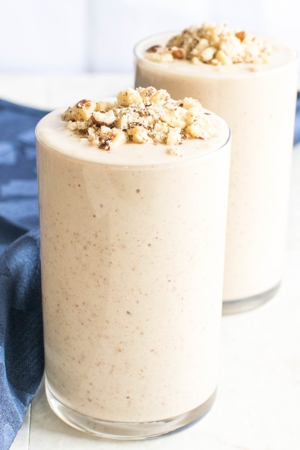 Two tall glasses filled with Hazelnut Cheesecake Smoothie and topped with crushed toasted hazelnuts is shown