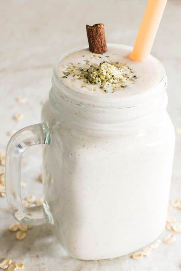 A tall serving glass filled with Oatmeal Creme Pie Smoothie and topped with hempseeds and a cinnamon stick