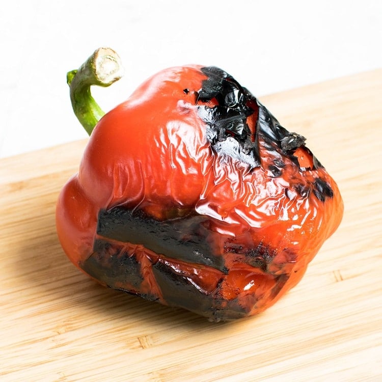 Roasted whole red bell pepper on a wooden board