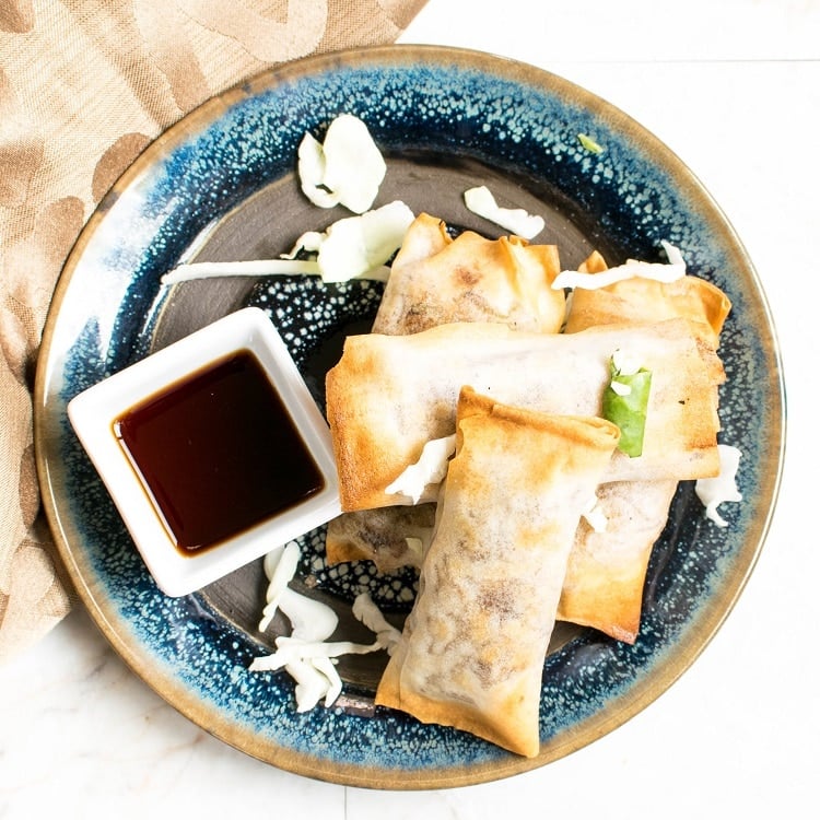 Top view of Air Fryer Vegan Spring Rolls on a blue plate and a brown table cloth as the prop