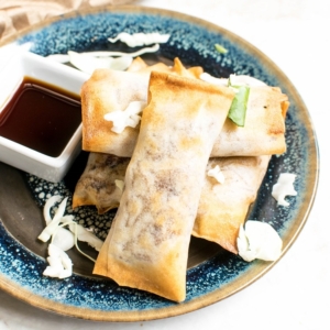 A blue plate stacked with Air Fryer Vegan Spring Rolls with a side of sauce