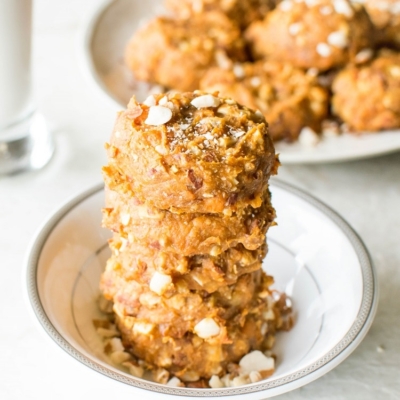 A stack of Peanut Butter Sweet Potato Cookies in a white small bowl with more cookies and a glass of milk as the prop