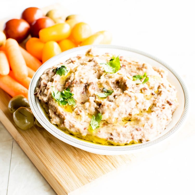 A bowl filled with red bean hummus dip and surrounded by veggies to complement it.