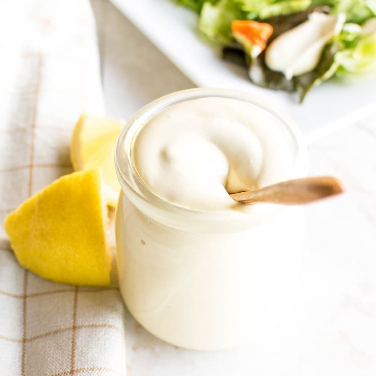 A glass container with Oil Free vegan Mayo and salad at the background