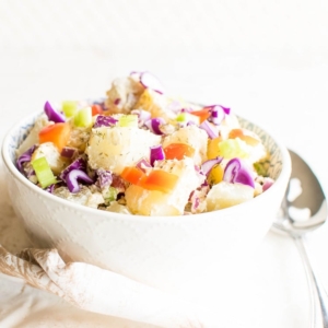 A close up front view of healthy vegan potato salad in a bowl with a large serving spoon as the prop