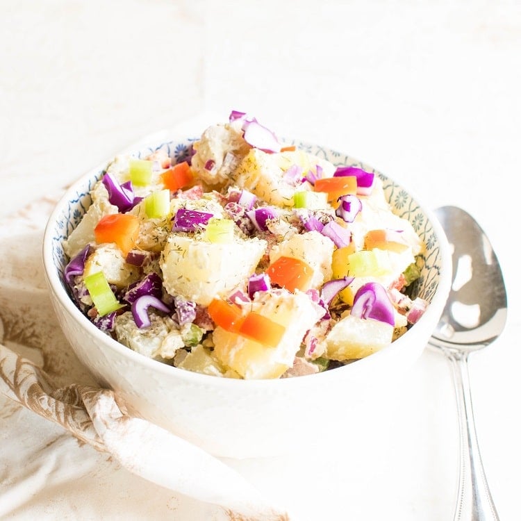 A 45 degree angle view of healthy vegan potato salad in a serving bowl with a large serving spoon on the side