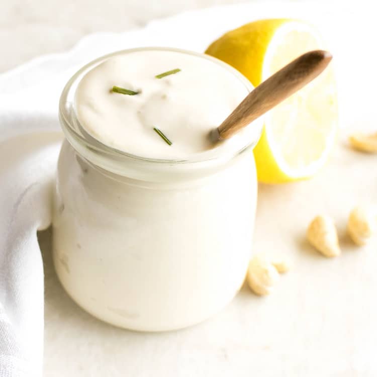 A 45 degree angle view of vegan sour cream along with a wooden spoon