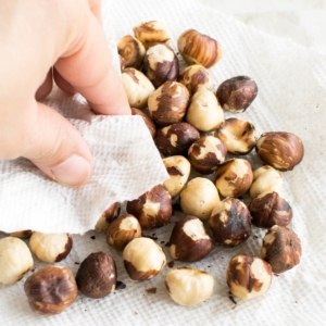 A hand rubbing the skin of hazelnuts