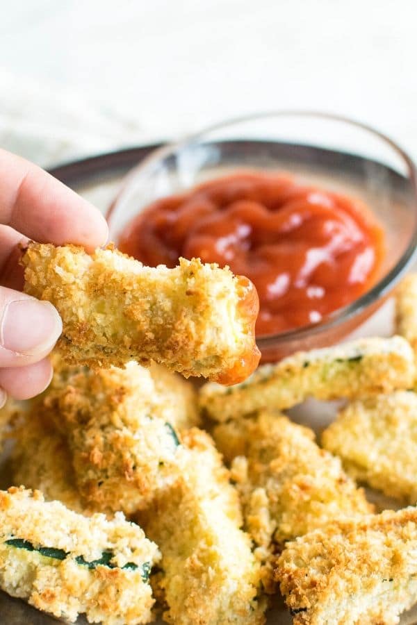 A hand picking up air fryer zucchini fries