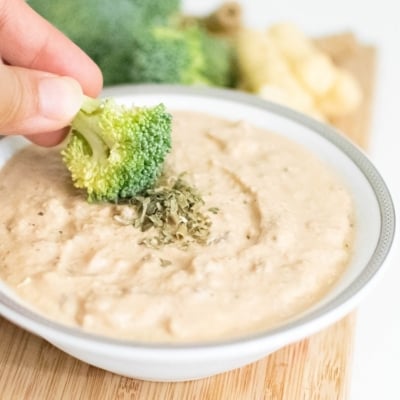 a hand showing the broccoli dipping into french onion dip recipe