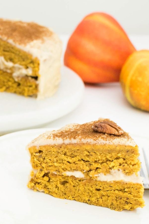 A slice of Pumpkin Cake Recipe with Quinoa Flour  served on a plate with the entire cake in the background.