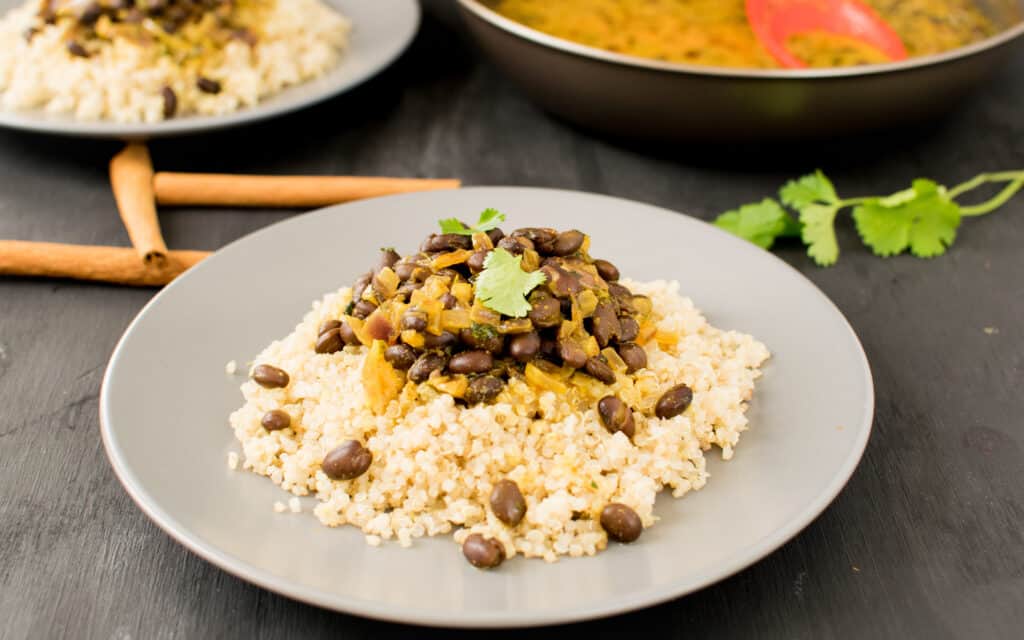 a front view of served black beans curry over quinoa with ingredients at the backdrop. 