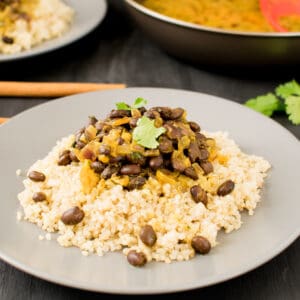 a front view of served black beans curry over quinoa with ingredients at the backdrop.