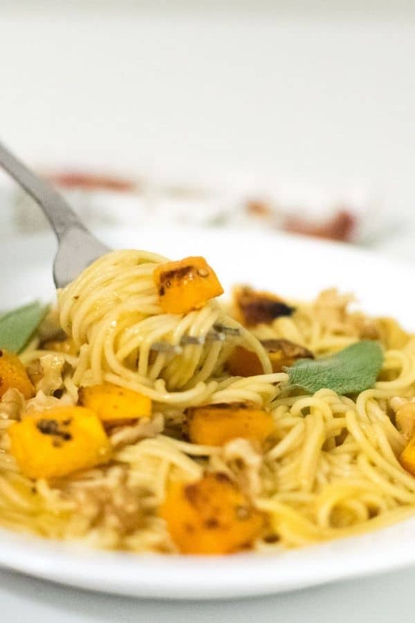 A fork picking up butternut squash pasta in focus.