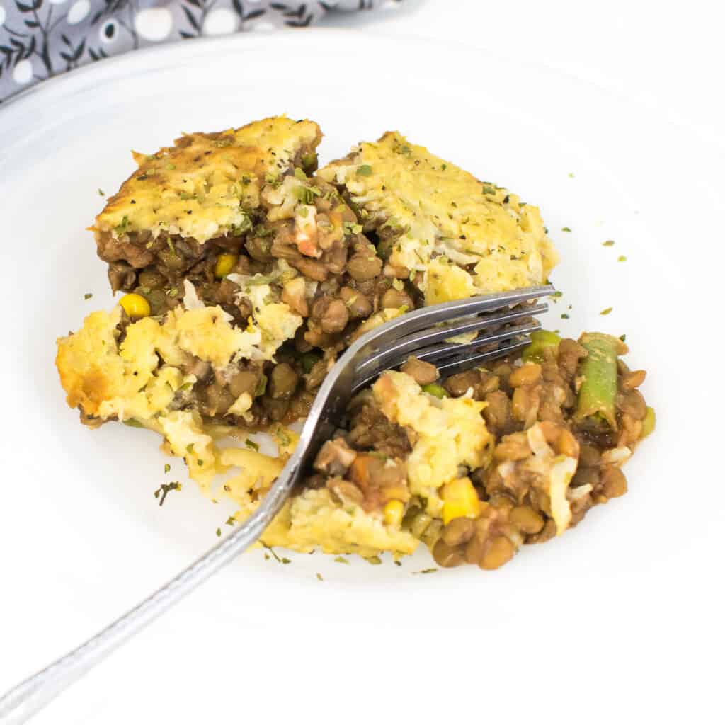 close up view of lentil shepherd's pie on a serving plate with a fork.