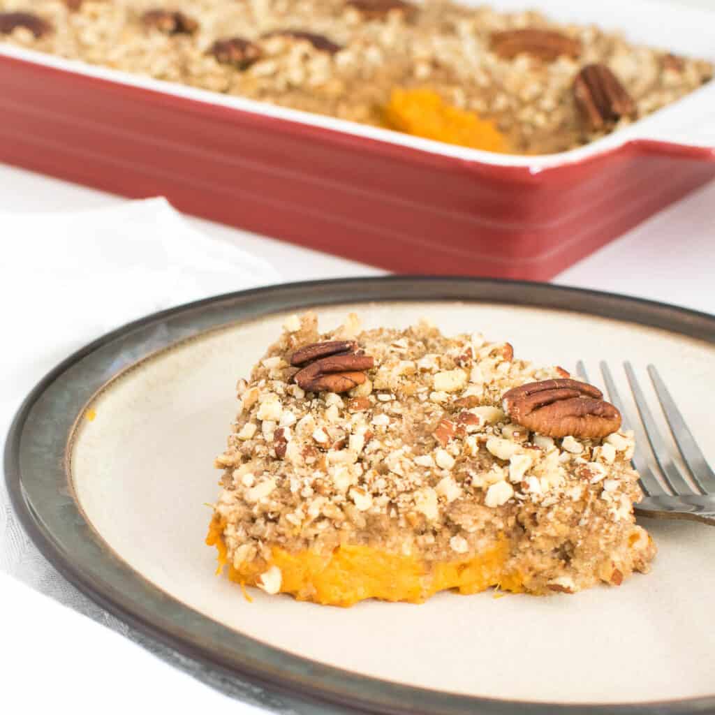 Vegan Sweet Potato Casserole served in a plate with the baking dish at the backdrop.