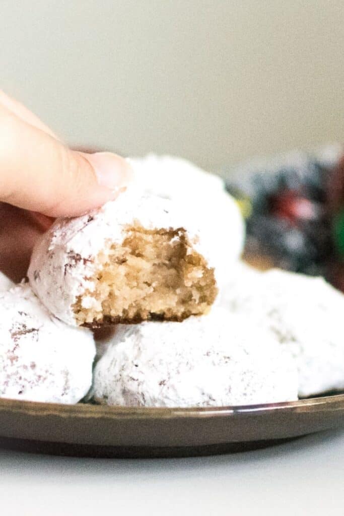 a hand picking up half eaten walnut snowball cookies (vegan).