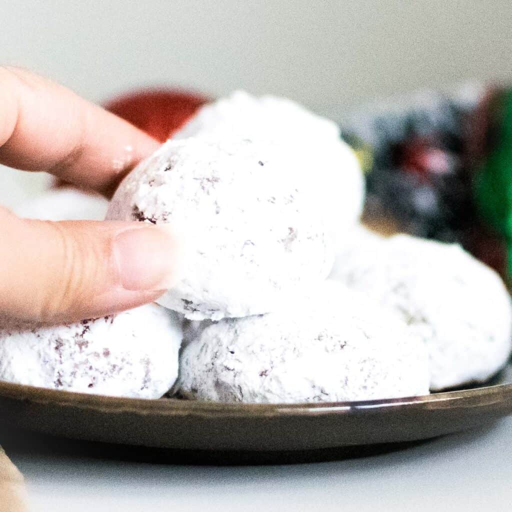 A hand picking up one of the walnut snowball cookies (vegan).