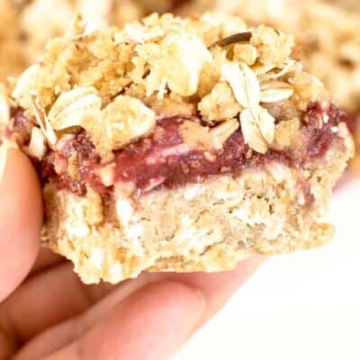 a hand holding a square piece of raspberry bars
