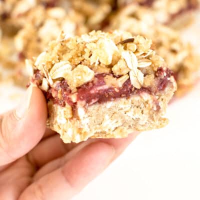 a hand holding a square piece of raspberry bars